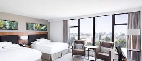 Habitación de hotel con dos camas, una mesita redonda pequeña, una silla y un escritorio con una lámpara.