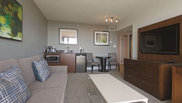 A compact living space with a kitchenette, a sofa with patterned cushions, a dining table, and a flat-screen TV mounted on a wooden cabinet.