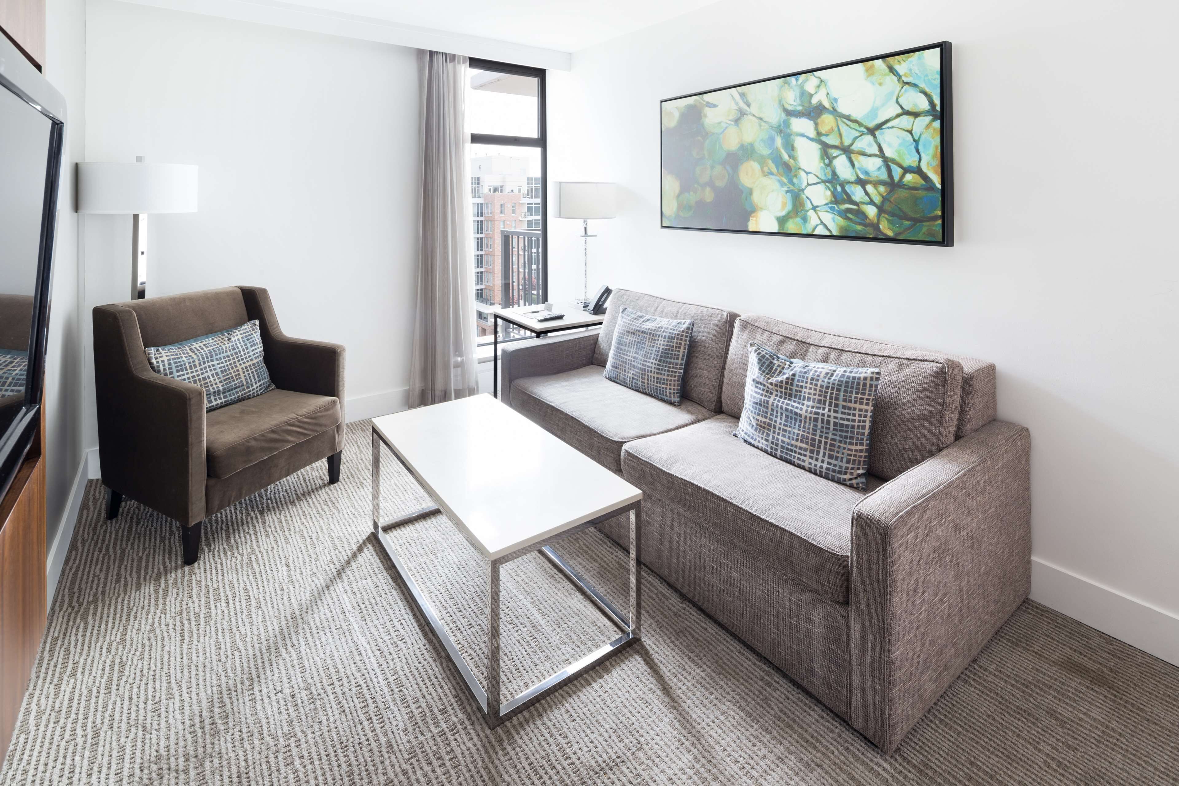 A modern living room with a sofa, armchair, coffee table, and a painting on the wall.