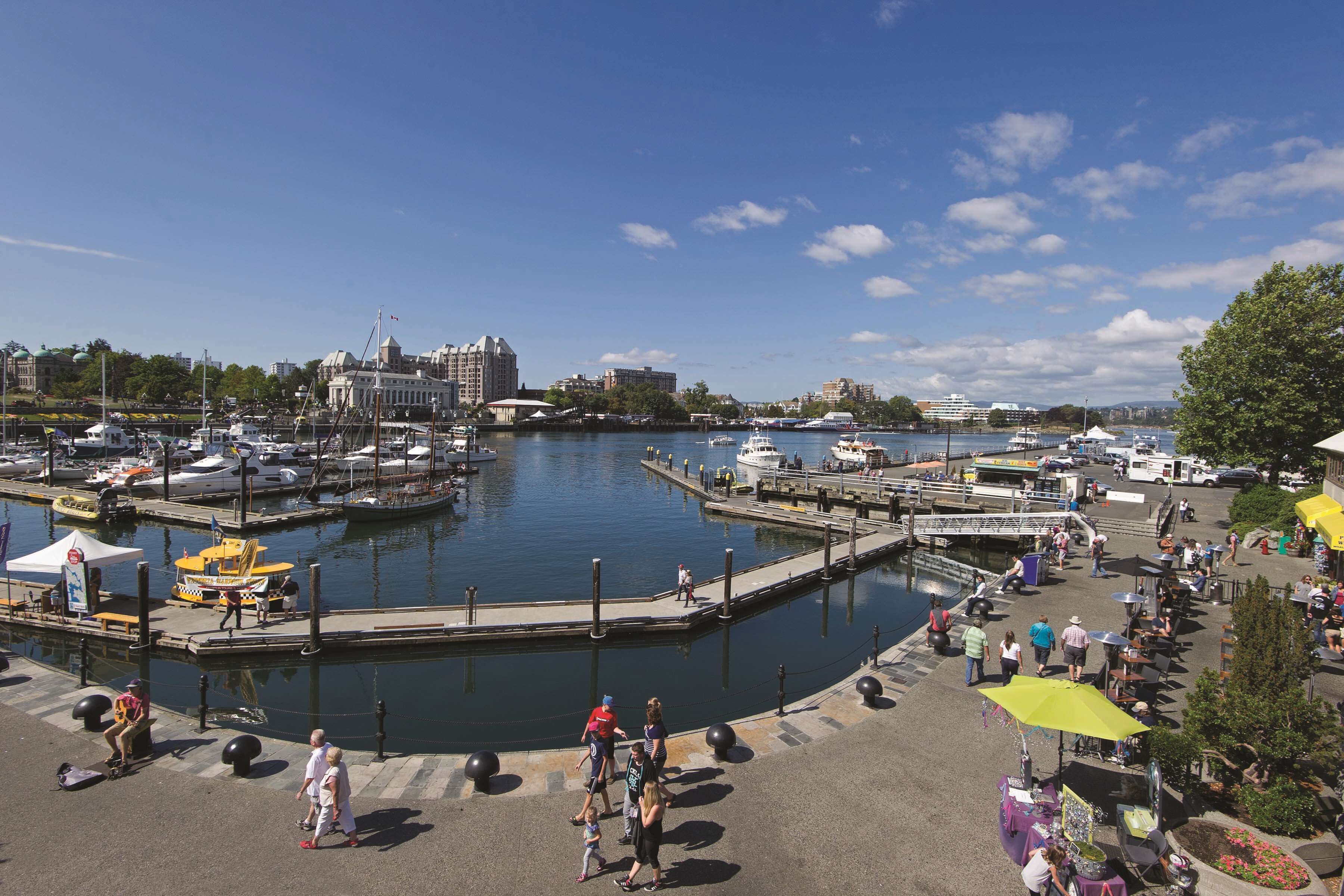 Un puerto deportivo con barcos amarrados, un paseo marítimo y un paisaje urbano al fondo.