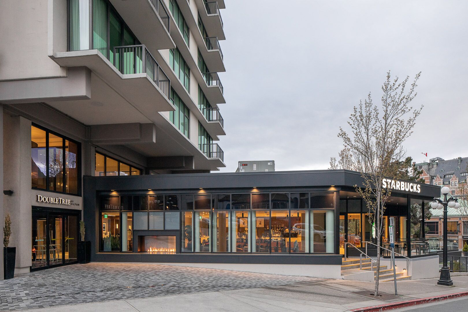 A modern building with a Starbucks on the ground floor, Doubletree hotel on the left, and a fire feature in the center.