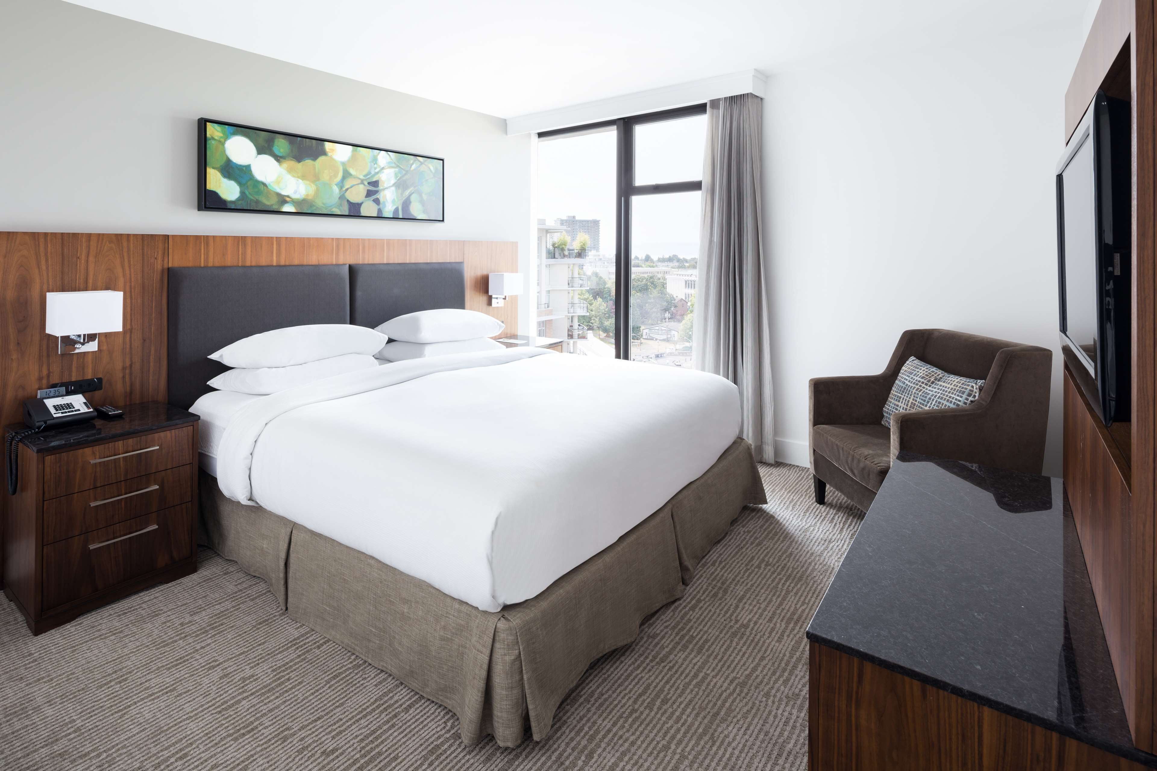 A hotel room with a large bed, a desk, a chair, a TV, and a window with a city view.