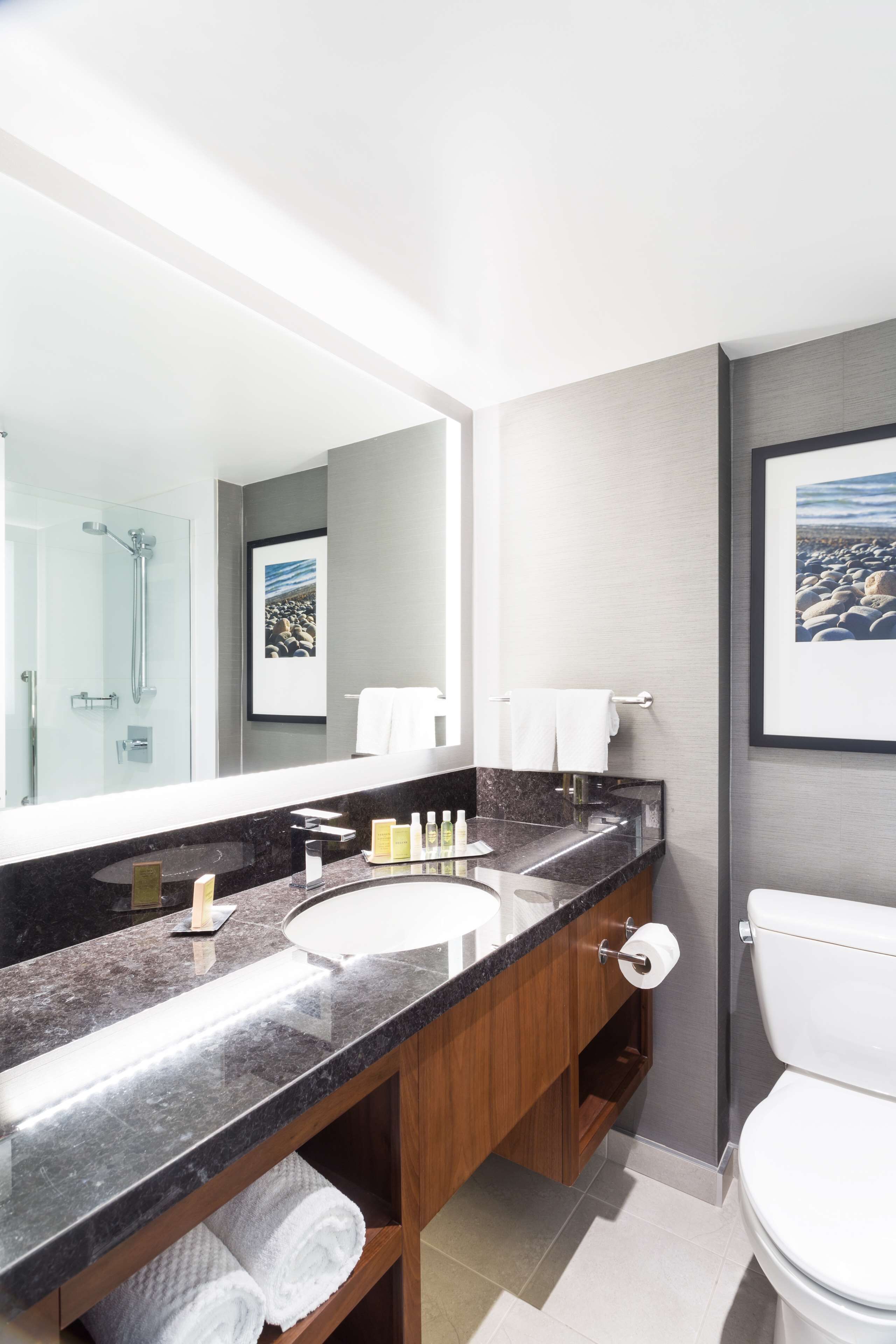 A modern bathroom with a large mirror, dual sinks, a toilet, and a shower.