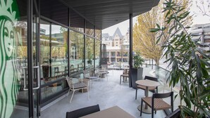 A modern outdoor seating area with glass walls, tables, and chairs, overlooking a cityscape. - DoubleTree by Hilton Hotel & Suites Victoria (Victoria)