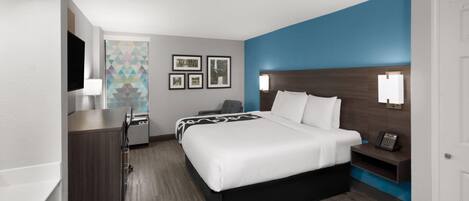 Una habitación de hotel con una cama, mesitas de noche, un televisor y un escritorio con lámpara.
