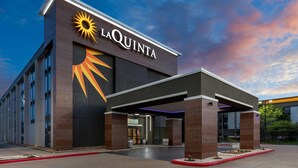 A hotel exterior with a prominent sun logo, a covered entrance, and a landscaped area with a red curb.