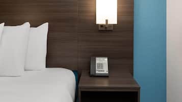 A neatly made bed with white linens, a bedside table with a lamp, and a control panel on the wall.