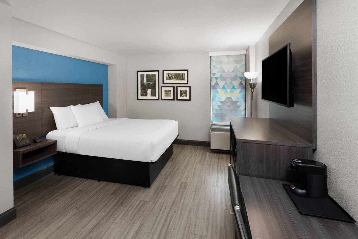 Een moderne hotelkamer met een bed, nachtkastje, lamp, televisie en een koffieapparaat.