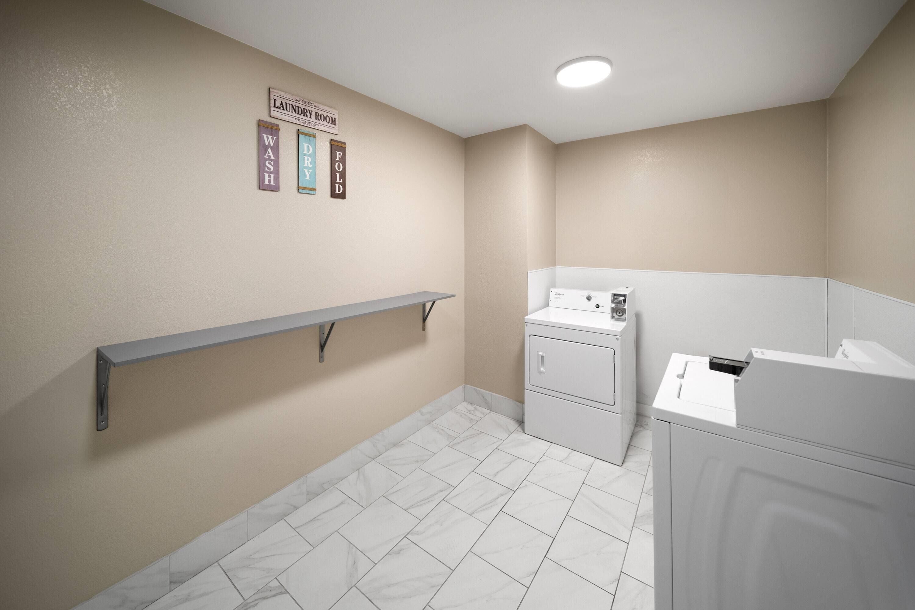 A laundry room with a washing machine, dryer, and a metal shelf.