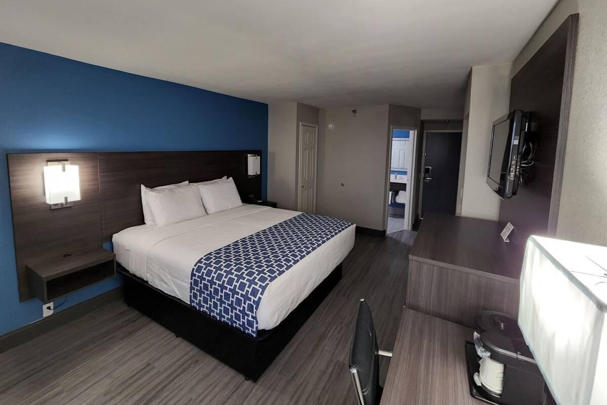Hotelkamer met een bed, nachtkastje, lamp, televisie en een badkamer zichtbaar door een geopende deur.