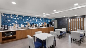 A modern cafe with a blue hexagonal wall design, wooden counter, and white tables with blue cushioned chairs.