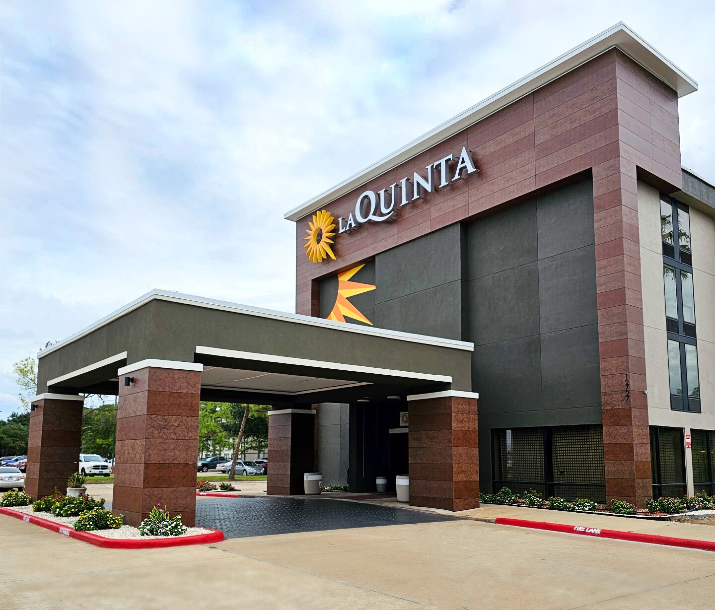 A hotel entrance with a modern design, featuring a prominent 'LA QUINTA' sign and a covered walkway.