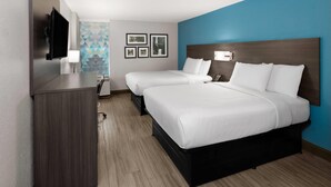 A hotel room with two beds, a desk, a TV, and a wall with framed pictures.