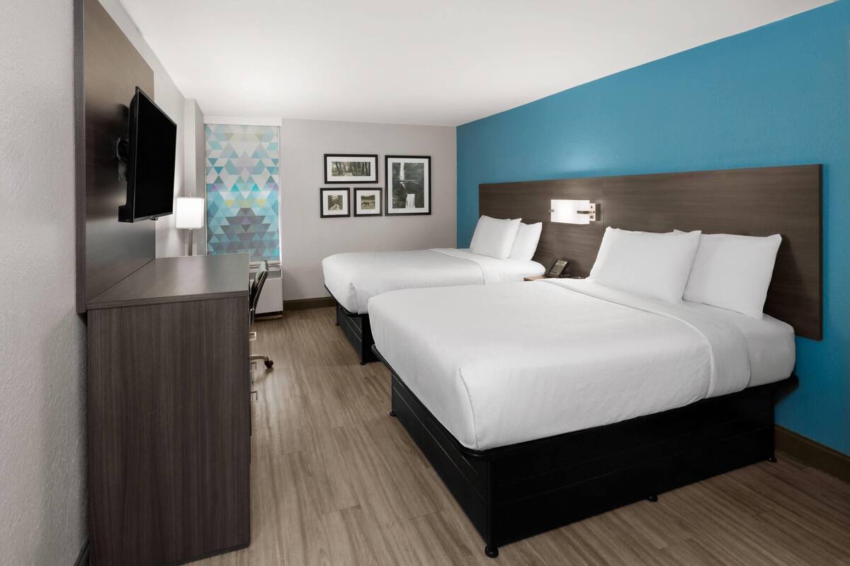 Een hotelkamer met twee bedden, een bureau, een televisie en een muur met ingelijste foto's.