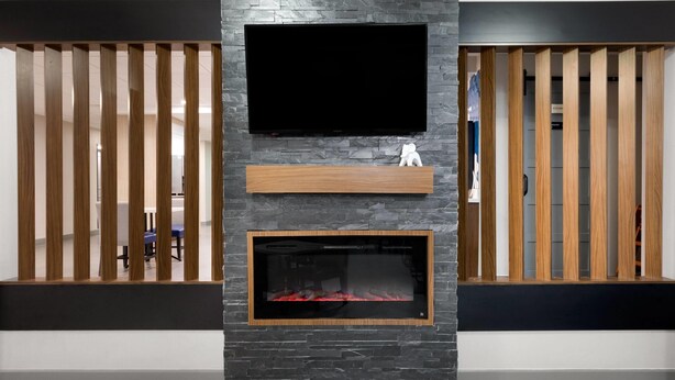 A modern living room with a flat-screen TV mounted above a fireplace, flanked by wooden slats on either side.