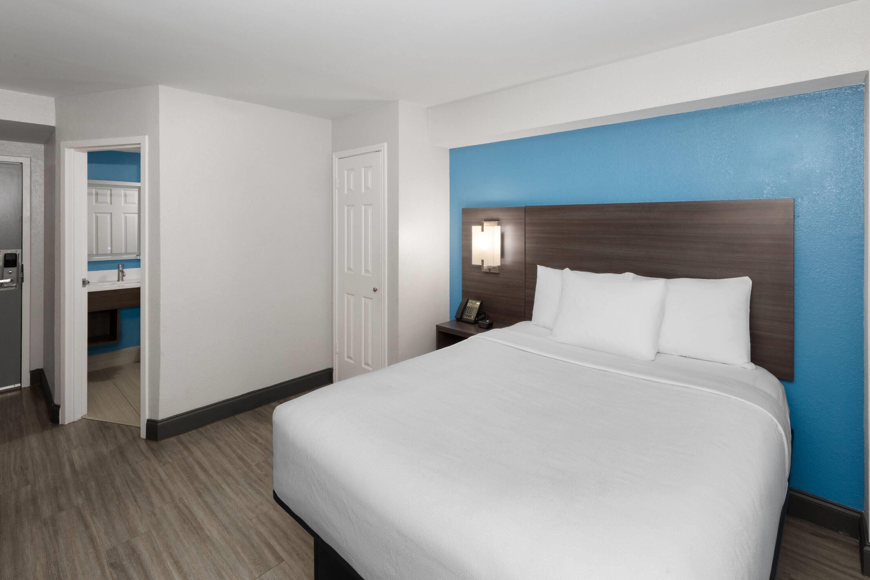 A hotel room with a large bed, a nightstand with a lamp, and a bathroom visible through an open door.