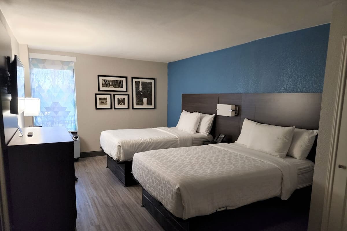 Een hotelkamer met twee bedden, een bureau, een telefoon en lijstjes met foto's aan de muur.