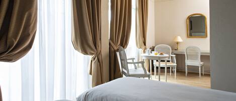 A hotel room with two beds, a dining area with a table and chairs, and a mirror on the wall.