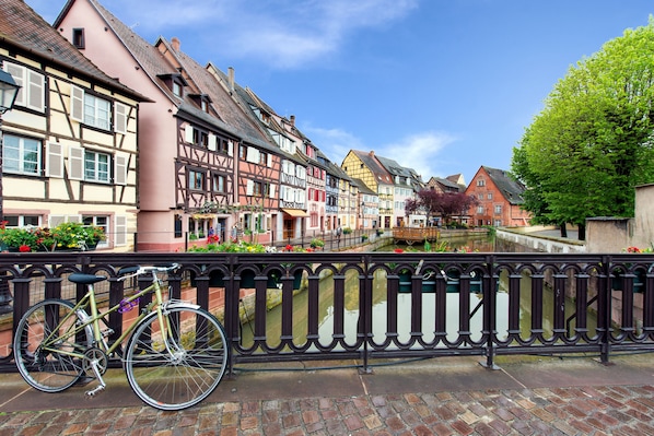 A row of traditional half-timbered houses along a canal with a bicycle parked on a bridge. - Grand Hotel Bristol By Stay Collection (Colmar)