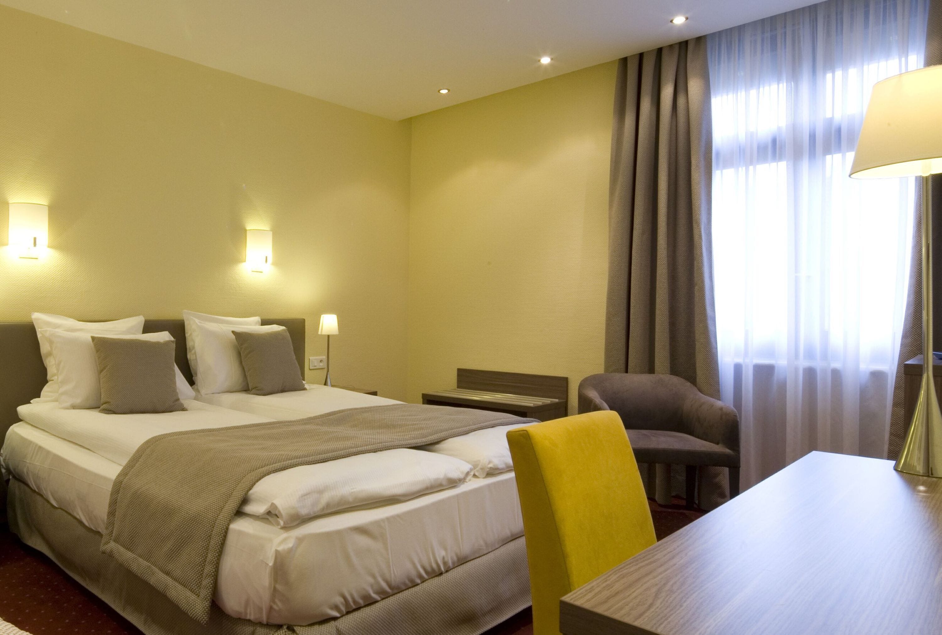 A hotel room with a bed, a desk, a chair, and a lamp.