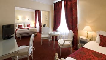 Habitación de hotel con cama, escritorio con televisor, dos sillas, una mesita y mesita de noche con lámpara.