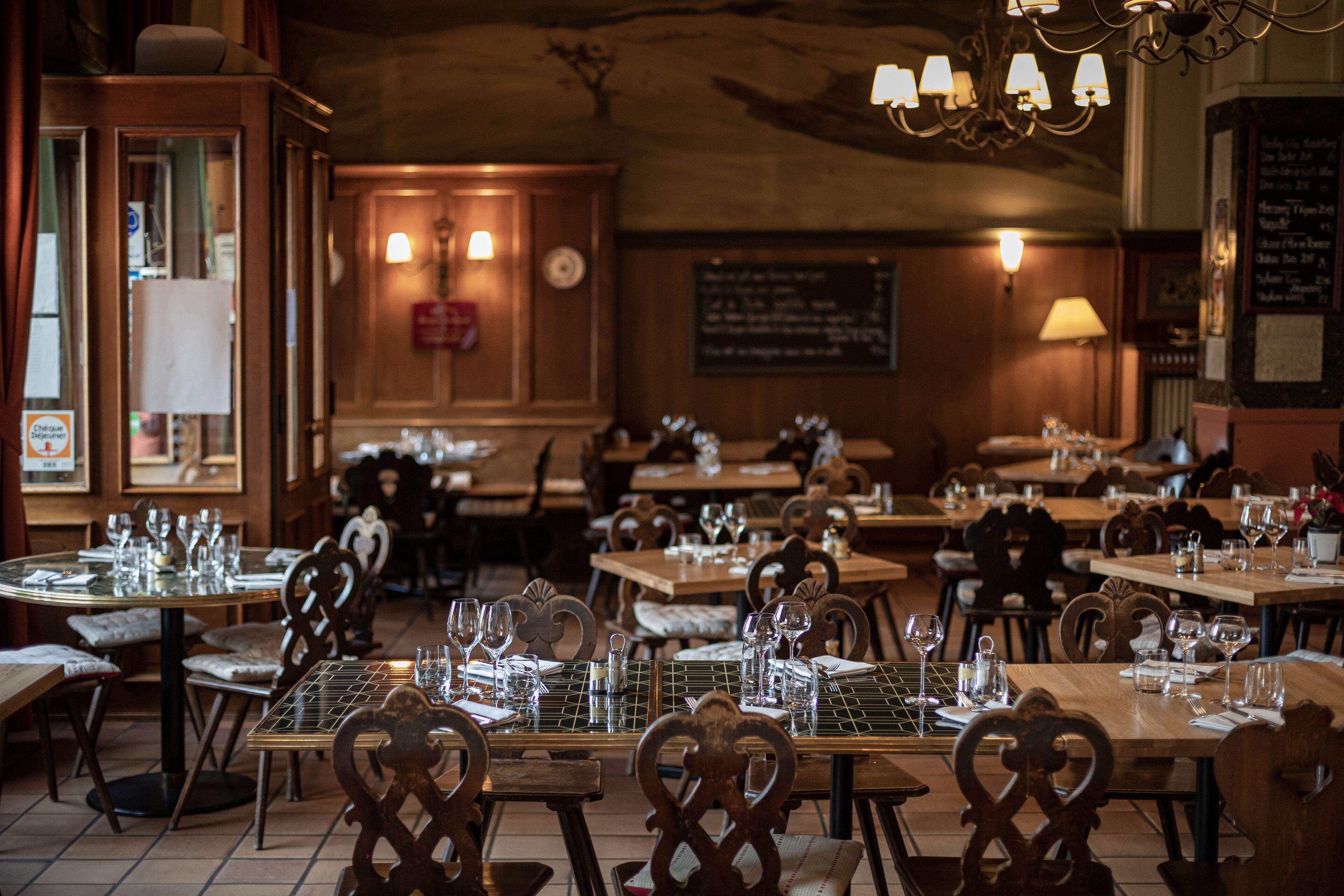 A restaurant with wooden tables and chairs, equipped with wine glasses and cutlery.