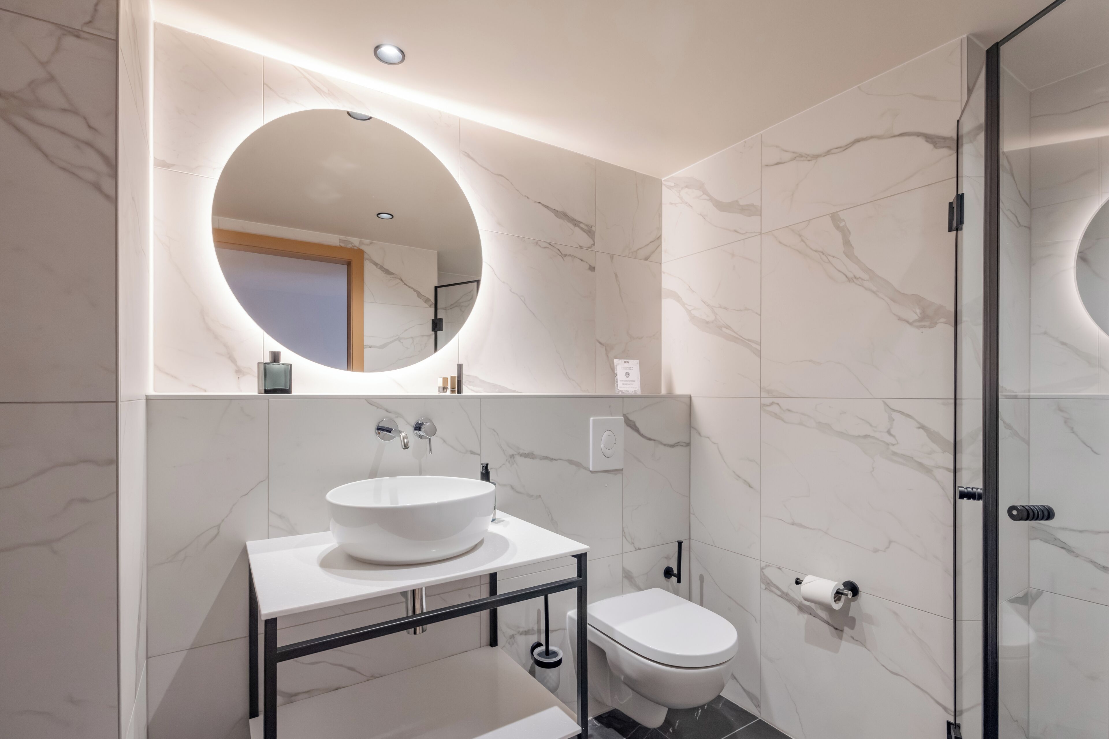 A modern bathroom with a round mirror, a white sink, and a toilet.
