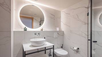A modern bathroom with a round mirror, a white sink, and a toilet.