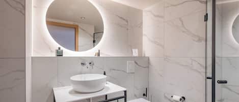 A modern bathroom with a round mirror, a white sink, and a toilet.