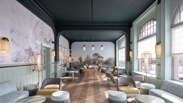 A spacious interior with a herringbone floor, seating areas, and large windows.