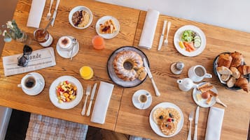 Een houten tafel met diverse ontbijtartikelen, zoals wafels, gebak en fruit.