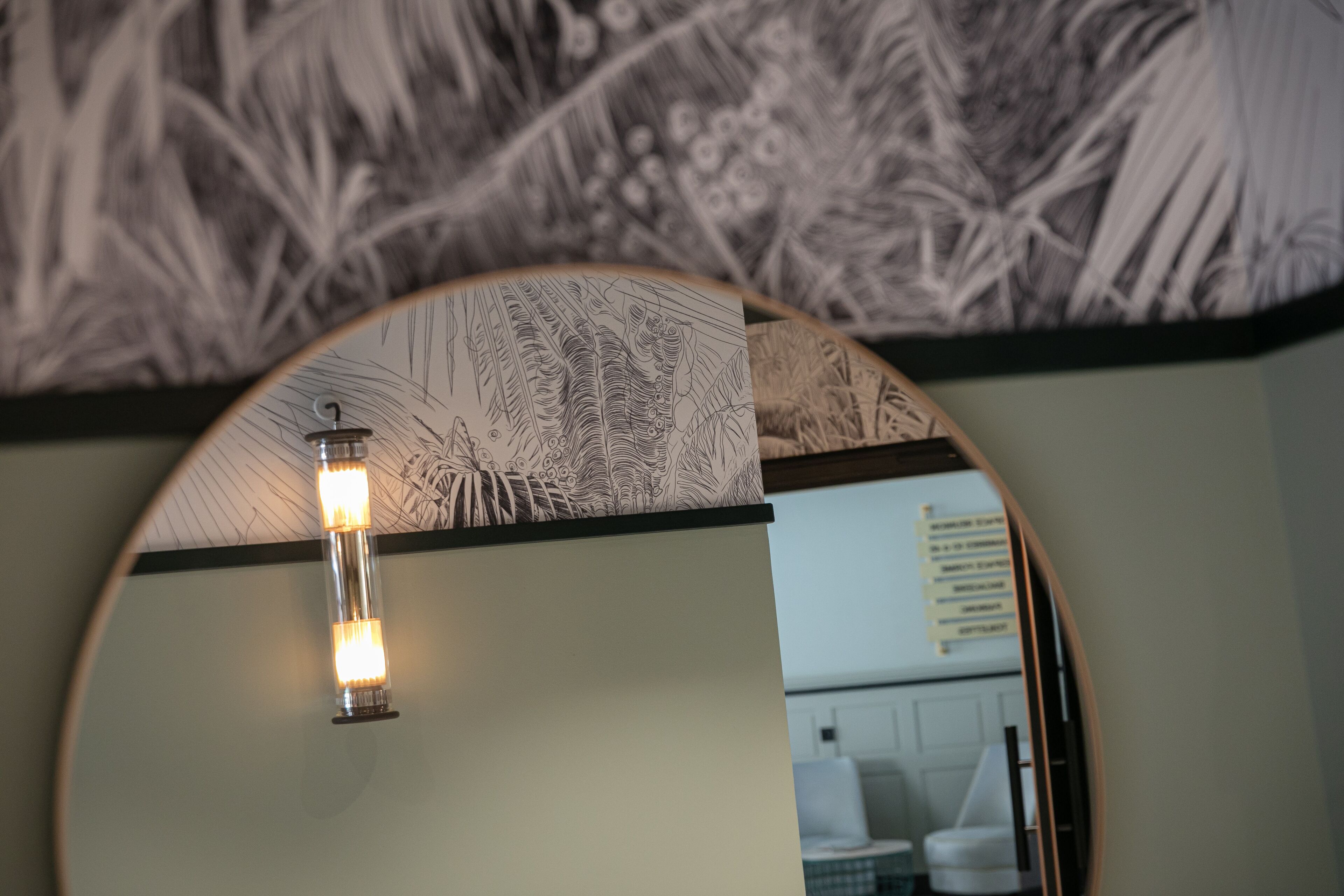 A circular mirror reflecting a room with a wall-mounted light fixture and a patterned wall.