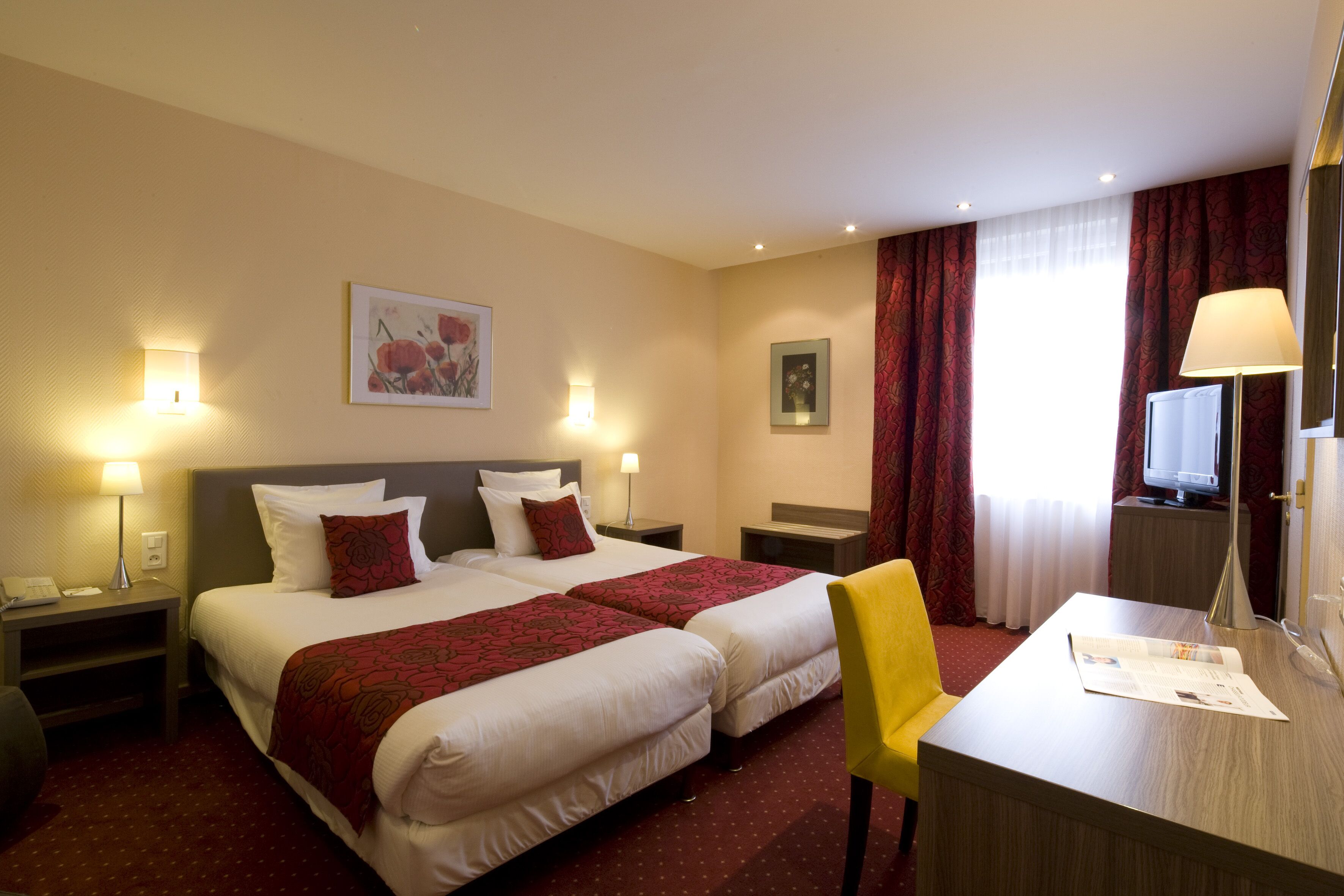 A hotel room with two beds, a desk, a chair, a TV, and artwork on the walls.
