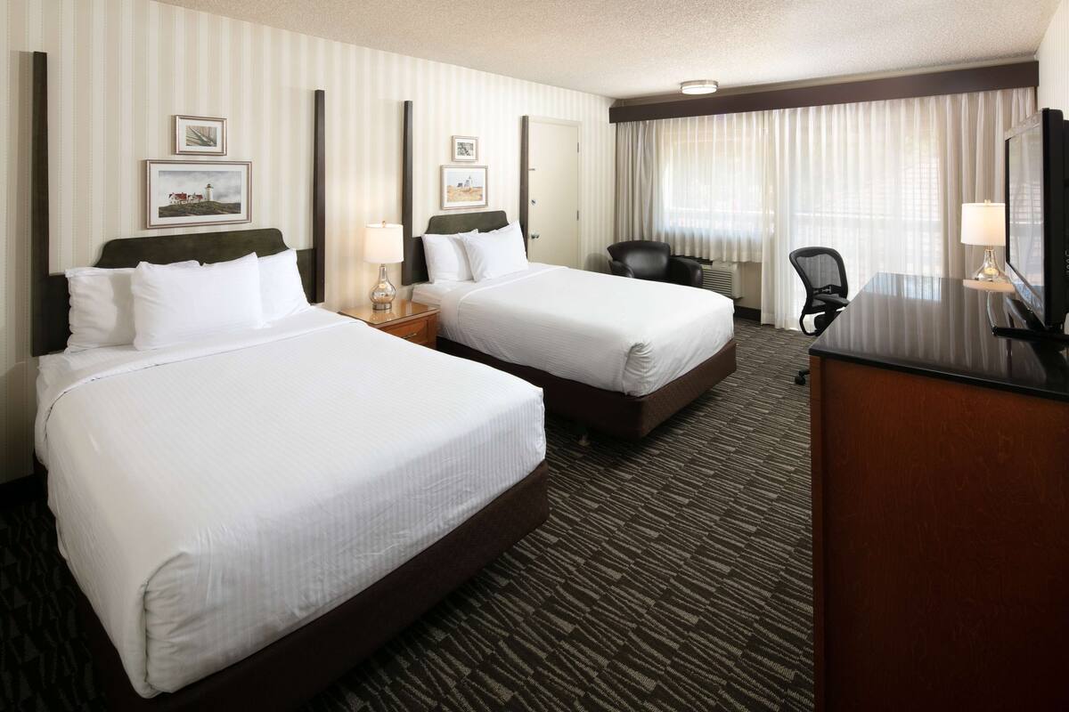 A hotel room with two beds, a desk, a chair, and a TV.
