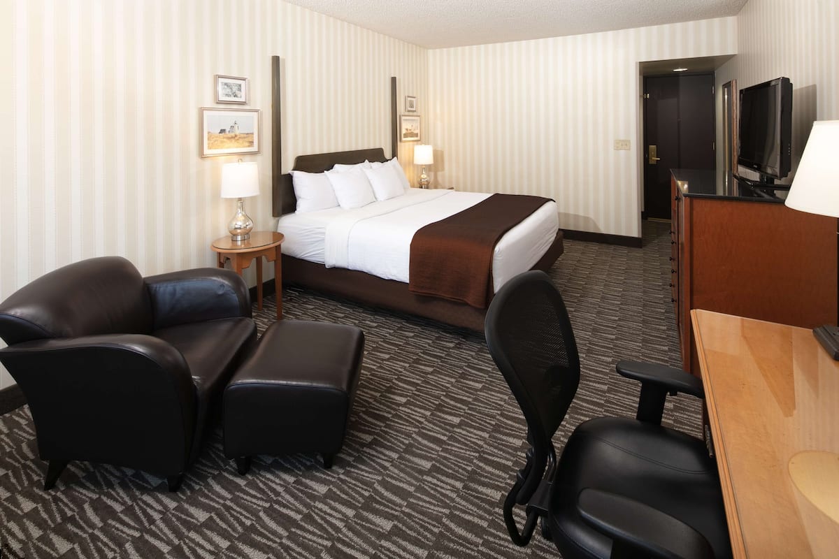 A hotel room with a bed, two chairs, a desk, and a TV.
