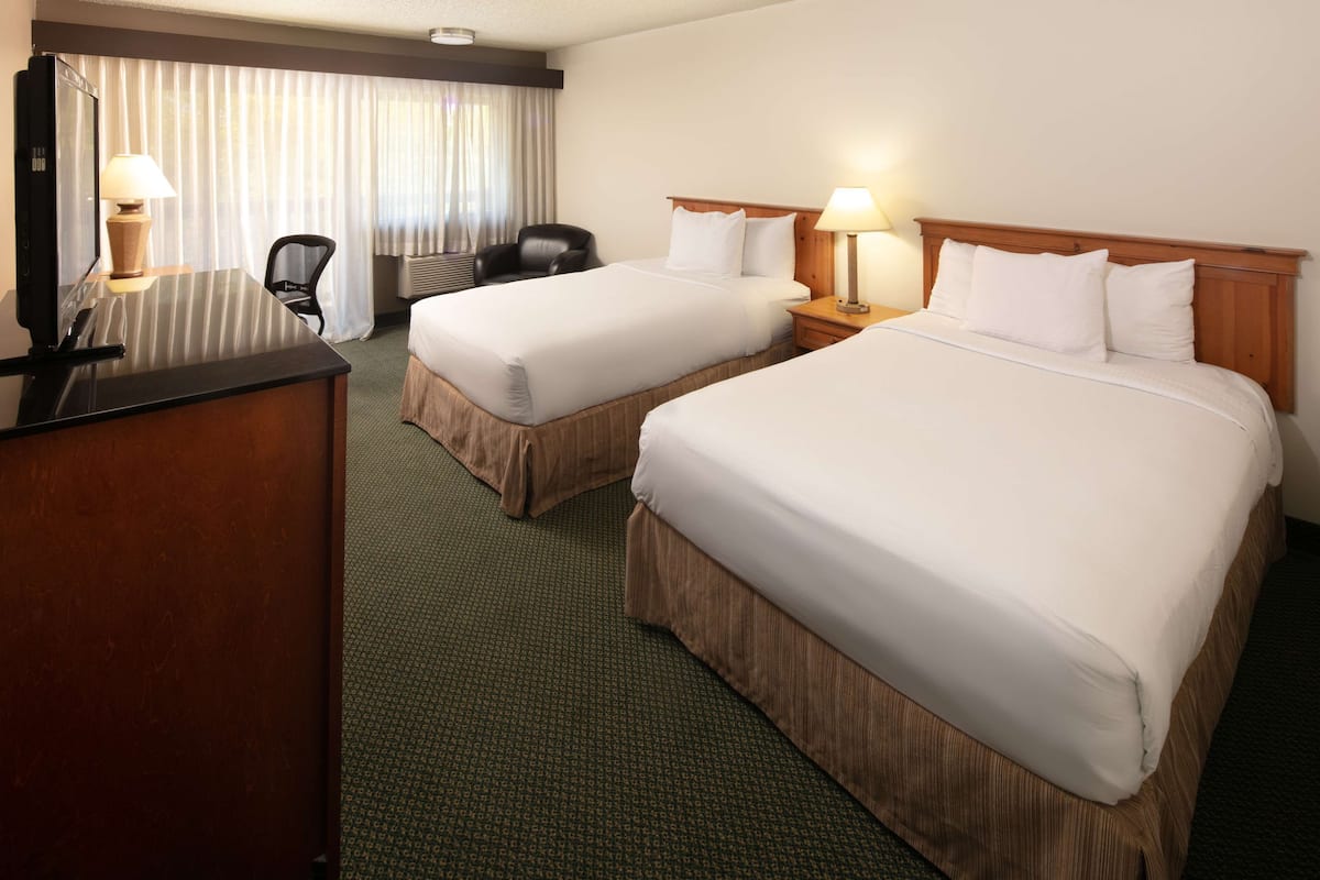 A hotel room with two beds, a desk, a chair, and a large window with curtains.