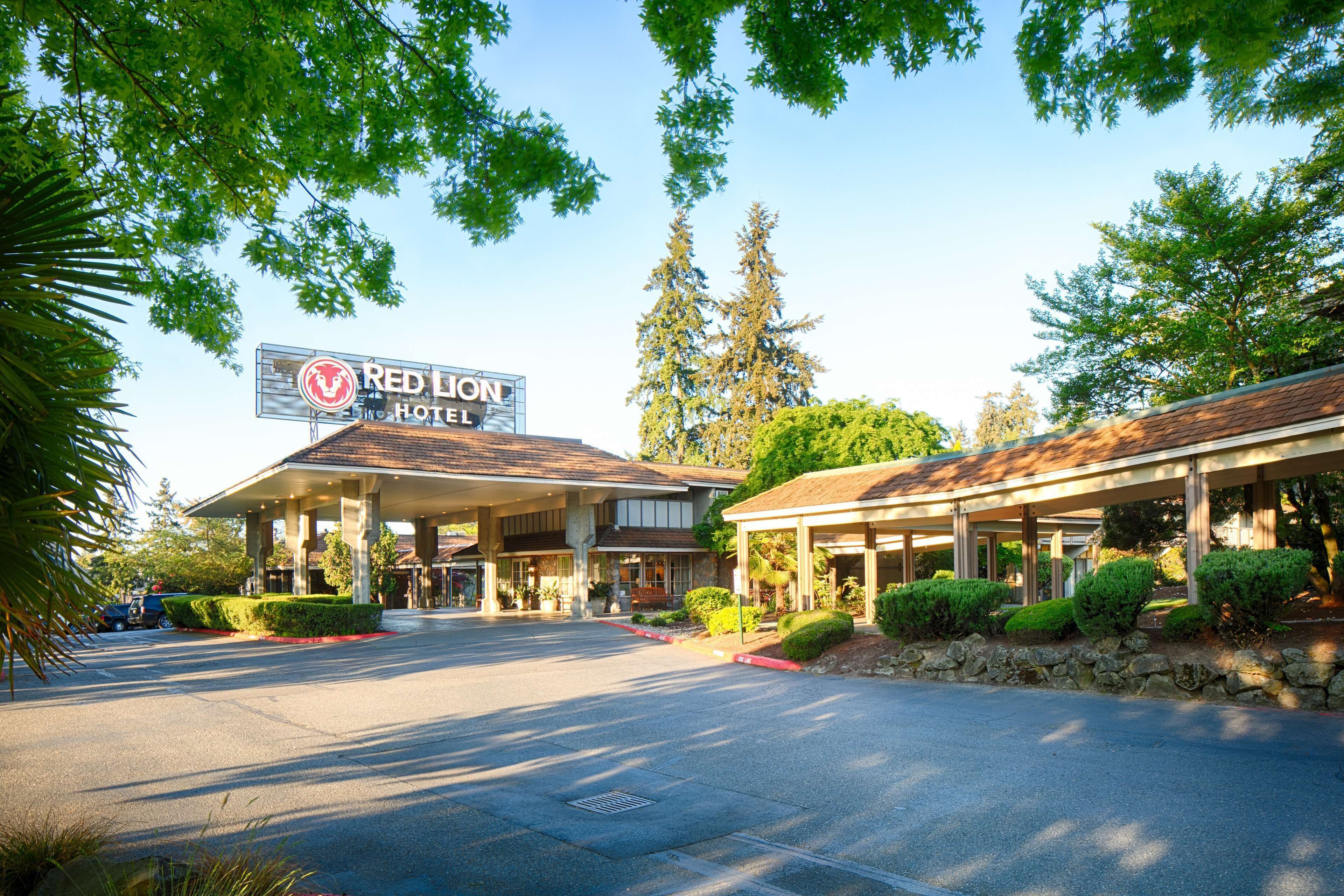 Un Hotel Red Lion con área de estacionamiento techada, una señalización y jardines bien cuidados.