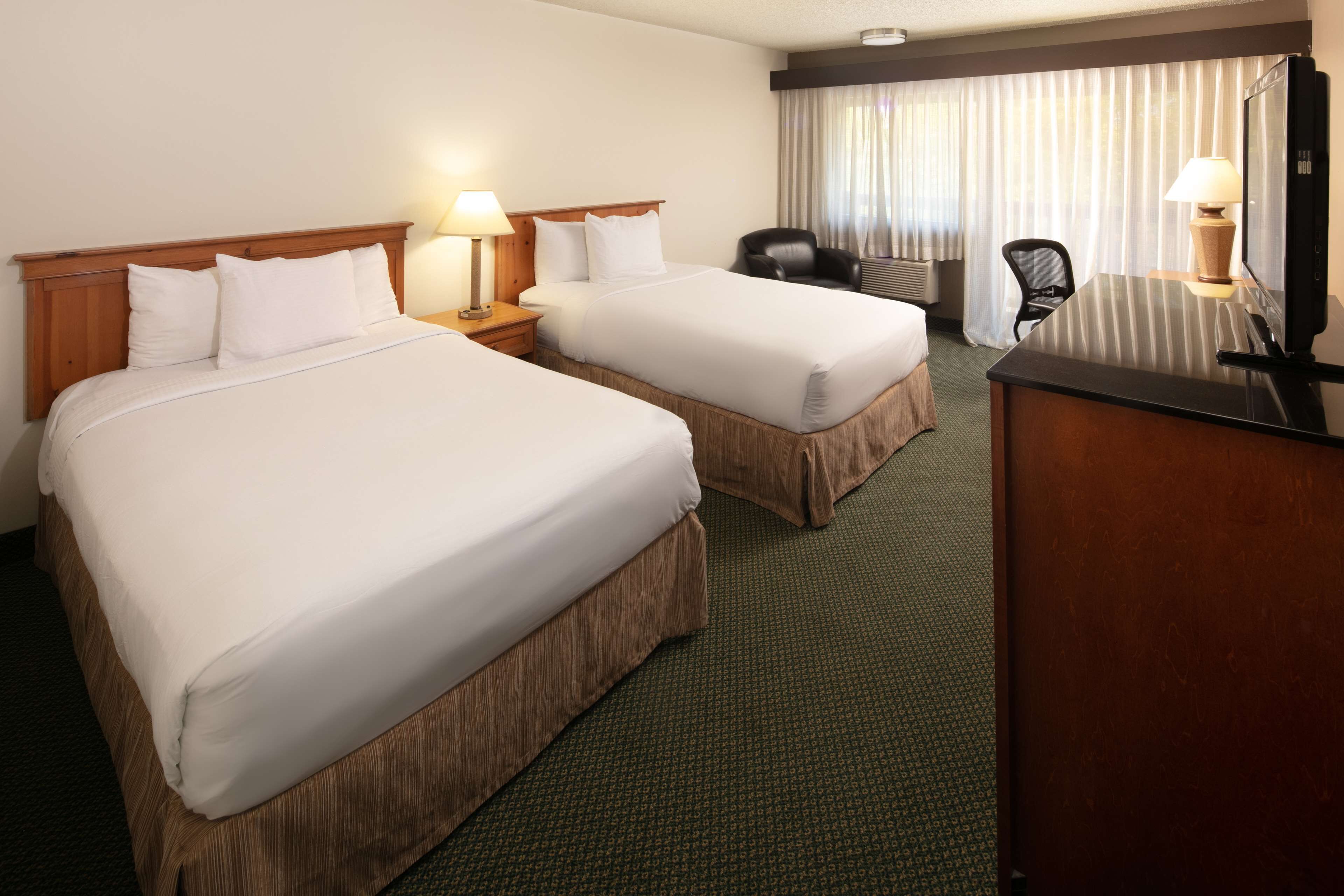 A hotel room with two beds, a desk, a chair, and a television.