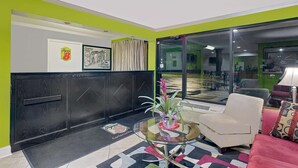 A modern lobby with a glass door, a reception desk, and a seating area with a red couch and a patterned pillow.