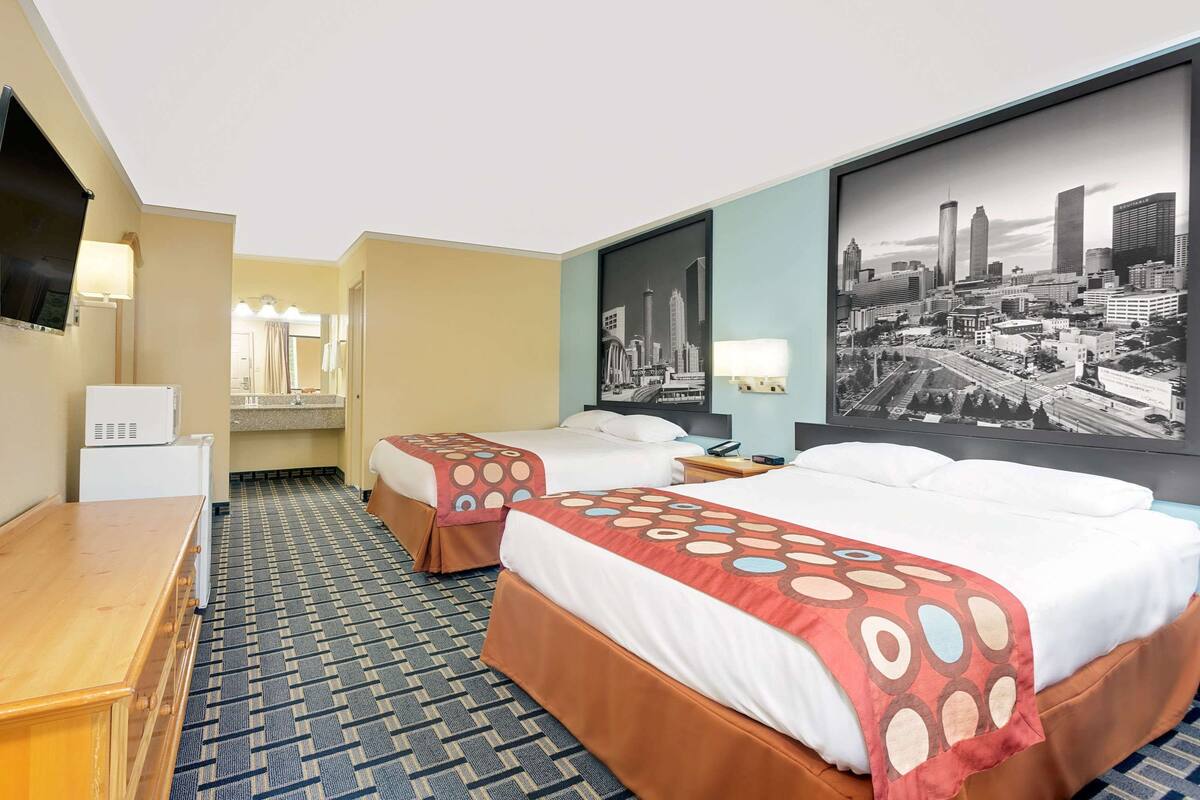 A hotel room with two beds, a desk, a TV, and a cityscape wall.