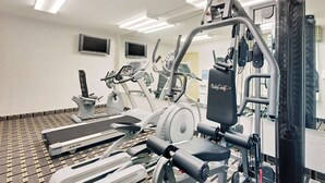 A gym with various exercise machines, a treadmill, and a mirrored wall.