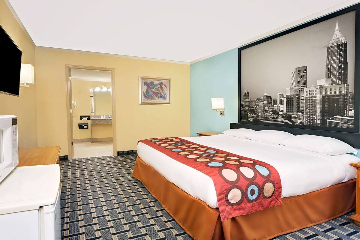 A hotel room with a large bed, a television, a desk, and a bathroom visible through an open door.
