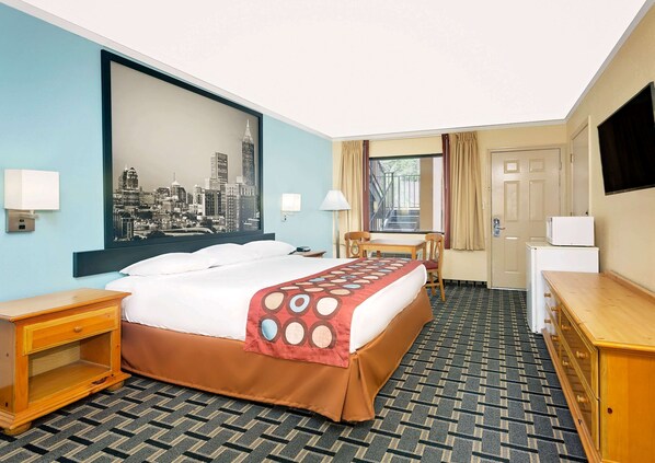 Une chambre d’hôtel avec un lit, un bureau, une chaise, une télévision et un tableau représentant un paysage urbain accroché au mur.