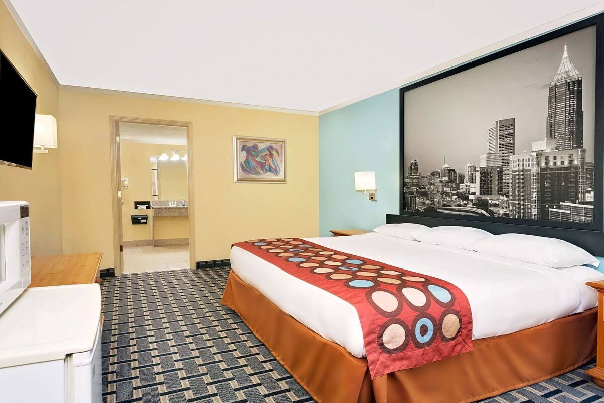 A hotel room with a bed, a desk, a television, a bathroom, and a cityscape view.