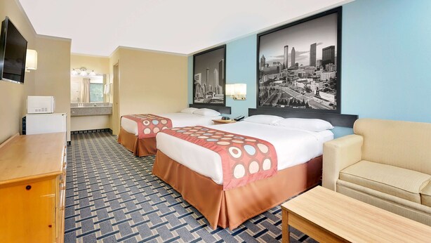 A hotel room with two beds, a sofa, a TV, and a cityscape painting on the wall.