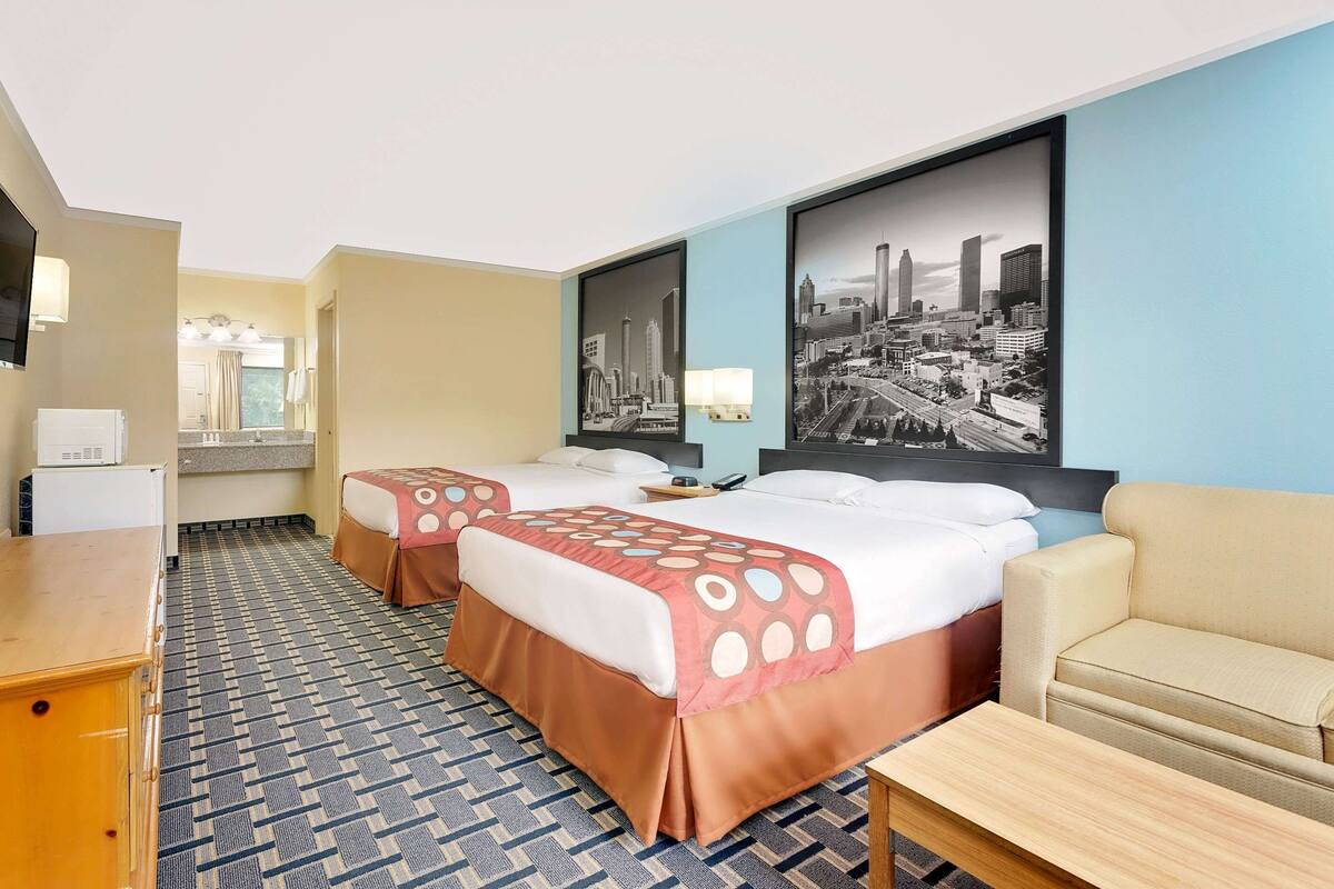 A hotel room with two beds, a sofa, a TV, and a cityscape painting on the wall.
