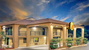 A two-story motel with a '13th Clearance' sign, featuring balconies, a parking lot, and landscaped areas.