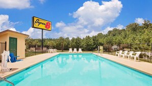 A swimming pool with a 'Super 8' sign, lounge chairs, and a fenced area with trees in the background.