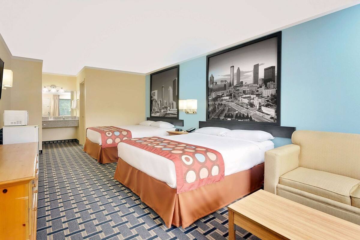 A hotel room with two beds, a sofa, a TV, a desk, and a cityscape painting.