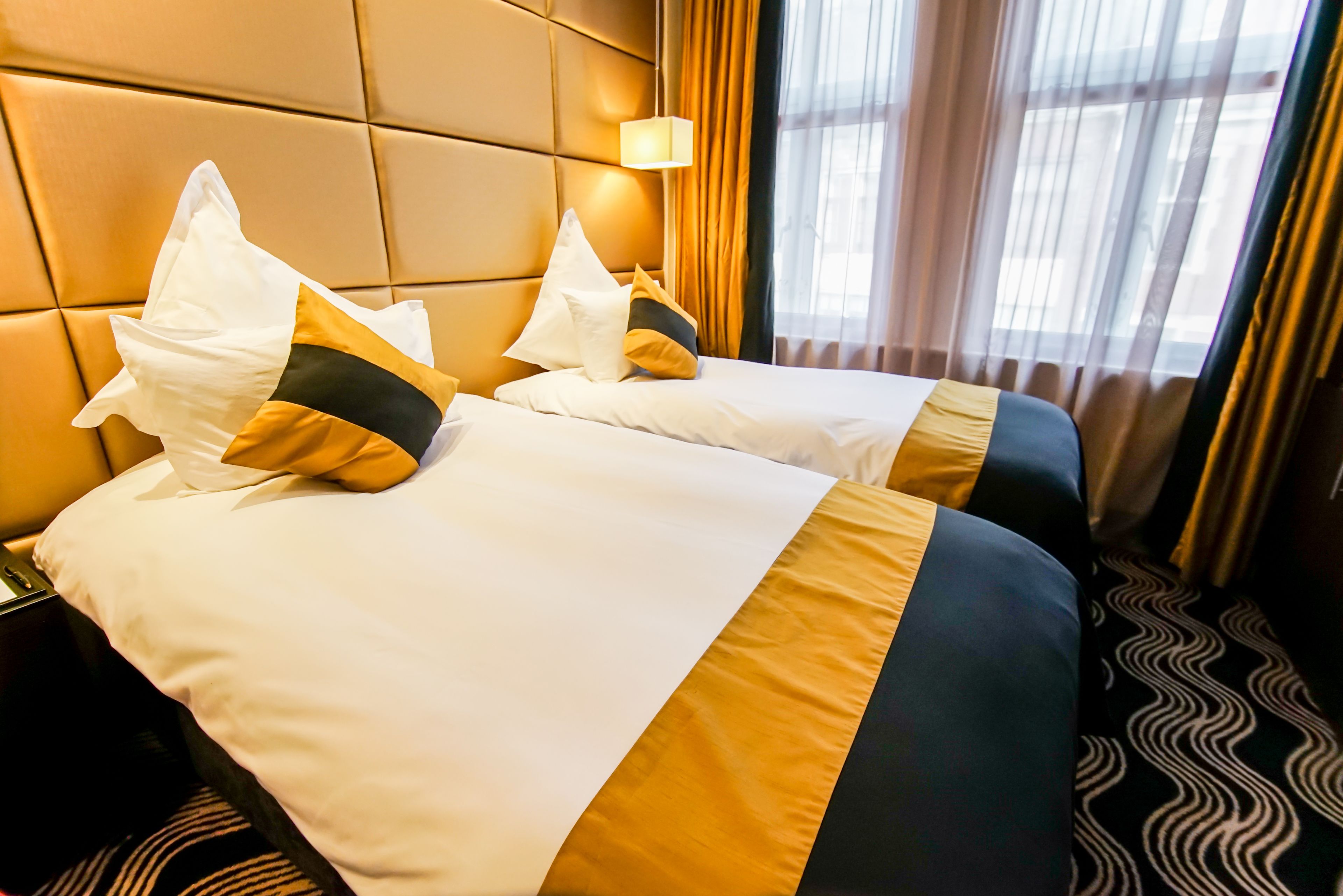 Une chambre d’hôtel avec deux lits, une tête de lit, une table de chevet, une lampe et une fenêtre avec des rideaux.